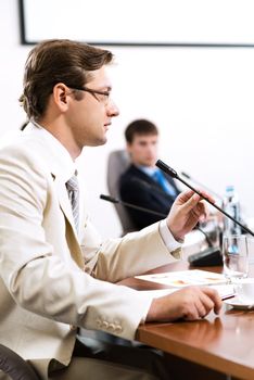 Portrait of a businessman, said into the microphone, in the background colleagues communicate with each other