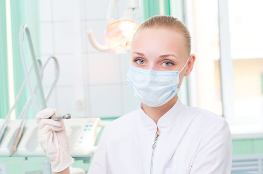 female dentists in protective mask holds a dental drill, the doctors at work