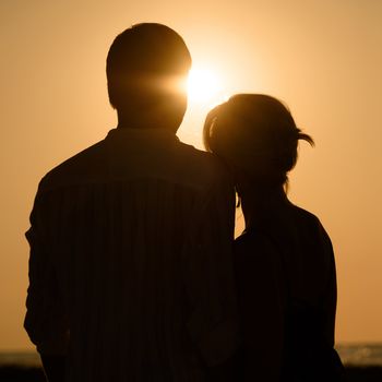 Silhouette of loving couple over orange sunset background 