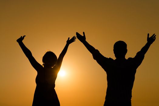 Silhouette of loving couple raise their hands with enjoy over orange sunset background 