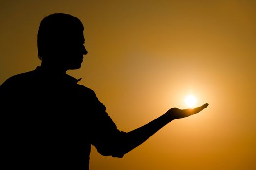 Silhouette of young man holding the sun on his hand at yellow sunset background