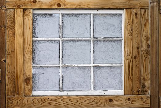 Horizontal image of an old wooden nine-lite window pane in a wooden wall, covered in ice crystals.