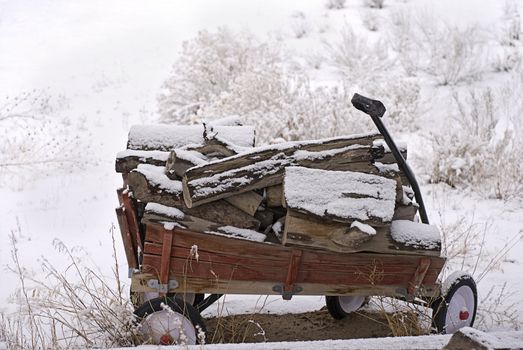 Wooden-sided red wagon loaded with firewood sits stranded in the snow after a snowstorm.