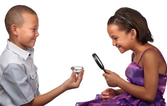 A young boy offers a large diamond to a young girl, who inspects it with a magnifying glass.