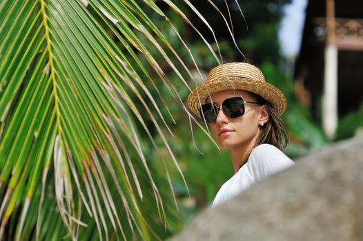 Woman in sunglasses near palm tree wearing hat