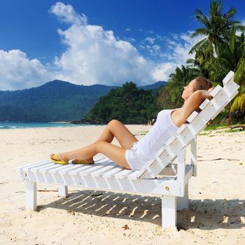 Girl on a tropical beach sitting at chaise lounge