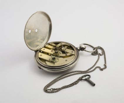 Antique pocket watch in silver with small key on a light background. Appearance with the clockwork.