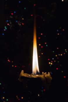 Burning candle on a dark background with small lights.