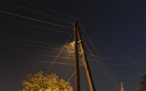 Image power pole with electrical wires, with street lamp and flight paths of moths at night.