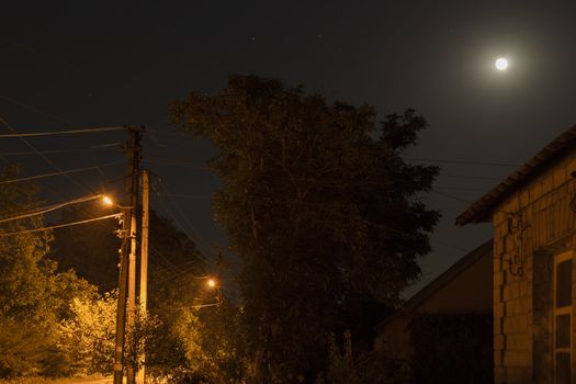 Image of a country road with the street lamps at night in clear weather with the moon and stars.