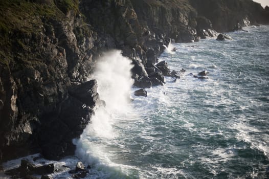 spray flying off a rock as a breaking wave crashes ashore on a rugded rock coastline