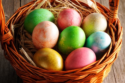 Colored easter eggs in basket on wooden table