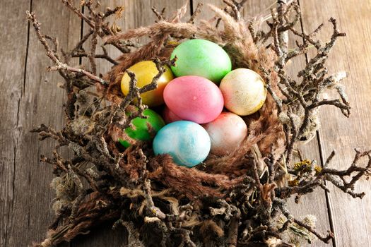 Colored easter eggs in nest on wooden table
