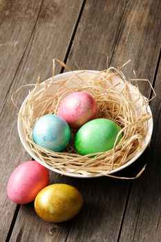 Colored easter eggs in nest on wooden table