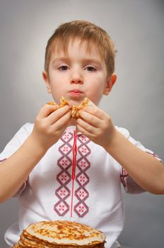 Russian little boy eats pancakes with red caviar.