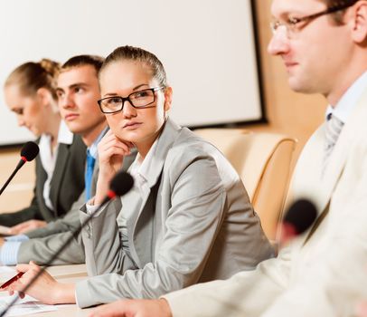 businessmen talking at the conference, sitting at the table, on the table microphones and documemts