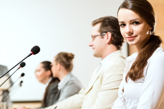 group of business people sitting at the tables at the presentation, woman looking at the camera