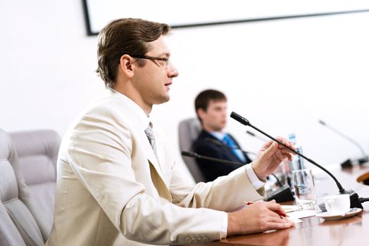 Portrait of a businessman, said into the microphone, in the background colleagues communicate with each other