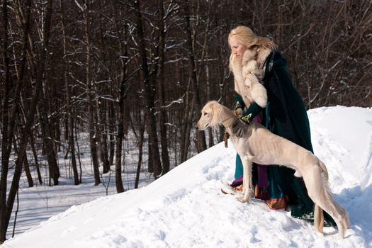 A blonde girl and a standing white saluki on snow
