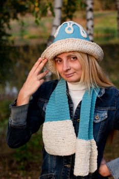 A blonde girl in a beret and scarf and jeans coat in a forest
