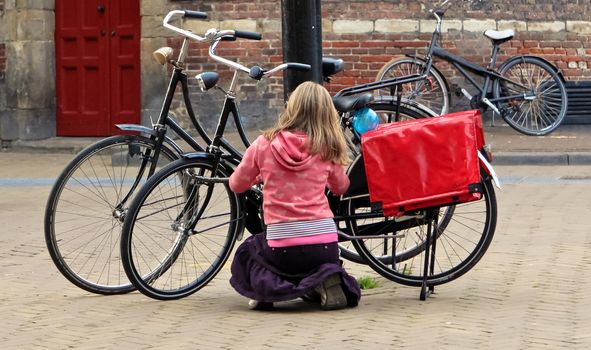 Blonde girl locking her bicycle whit a padlock at lamppost.
