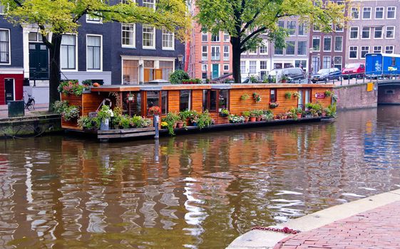 Precious wooden houseboat with flowers and plants in one canal of Amsterdam.