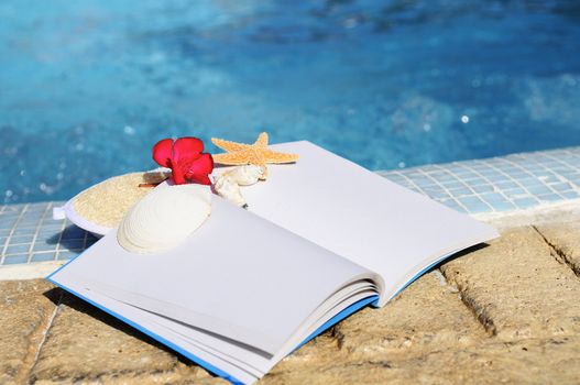 open book, shellfish and white towel beside a pool