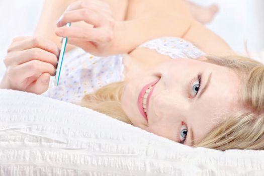 Cute woman lying in bed and polishing nails