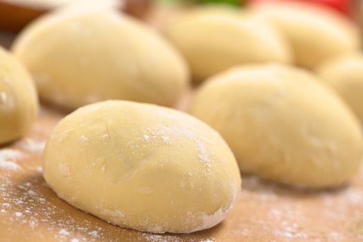 Small balls of fresh homemade pizza dough on floured wooden board (Selective Focus, Focus one third into the first pizza dough) 