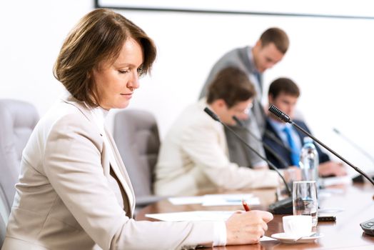 Senior business woman working with documents at the conference, on the table microphone stand