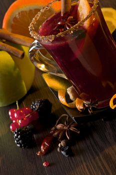 Glass of Mulled Wine with Cinnamon Stick, Slice of Orange and Anise Star closeup on Dark Wood background with Fruits and Spices  