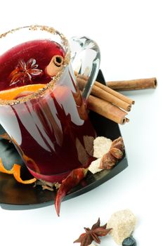 Glass of Mulled Wine with Cinnamon Stick, Slice of Orange, Anise Star and Spices on Black Saucer closeup on white background