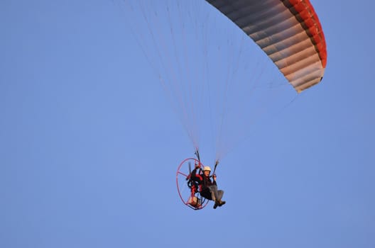 Photo shows a paraglider flies on a background of blue sky.