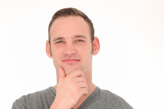 Happy thoughtful young man smiling as he stands with his hand to his chin isolated on white