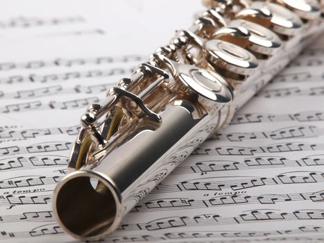 A used flute rests across an open musical score. Only one line of music is in focus.     