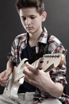 Photo of a young male playing the electric guitar. The young male is out of focus  and the headstock of the guitar is in focus.