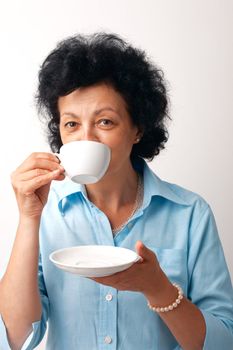 Portrait of an elder woman drinking from a cup and holding a saucer.