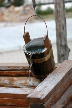 Wooden bucket over the well with flowing water