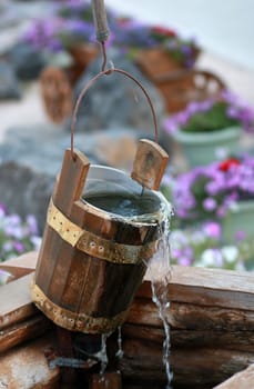 Wooden bucket over the well with flowing water and cobwebs