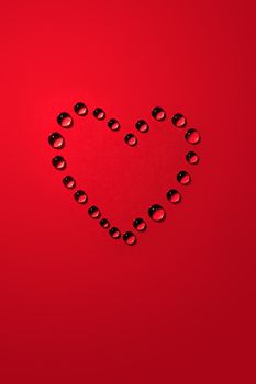 Love concept. Heart shape made from drops of water on red paper background