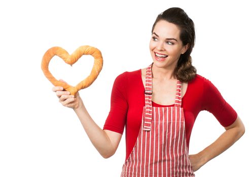 A beautiful woman wearing an apron smiling and holding and looking at a love heart made out of bread. Isolated on white.