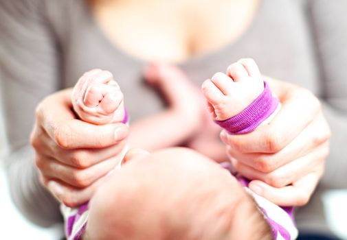 Overhead cropped view of a mother holding a tiny baby's hands in her own with focus to the hands