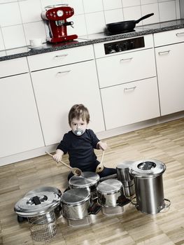 Photo of an adorable young boy using wooden spoons to bang pots and pans that are set up like a drumset. Desaturated and contrast increased.
