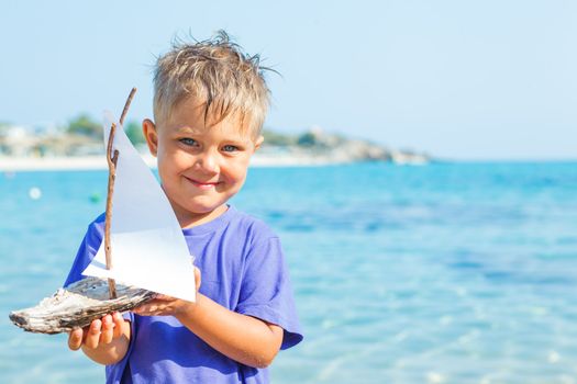 Cute boy with toy ship in hands ashore