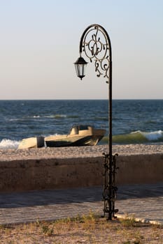 Forged park street lantern  on the beach with a boat and a pinnace on a summer morning