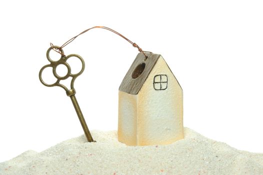 key and house model on the sand isolated on white