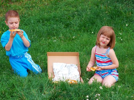 Picnic on the grass. boy and small girl  have a dinner with pizza on the meadow .