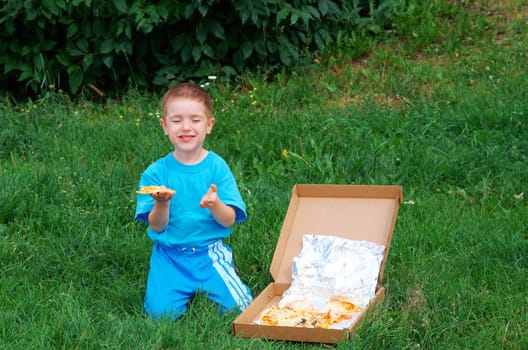 Picnic on the grass. boy   have a dinner with pizza on the meadow .