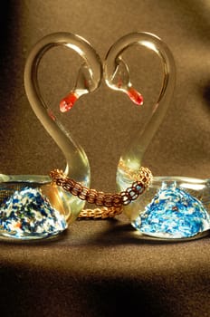 Figurine glass swans with a bright blue pattern,related gold chain on a black background