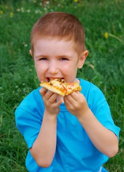 Picnic on the grass. boy   have a dinner with pizza on the meadow .